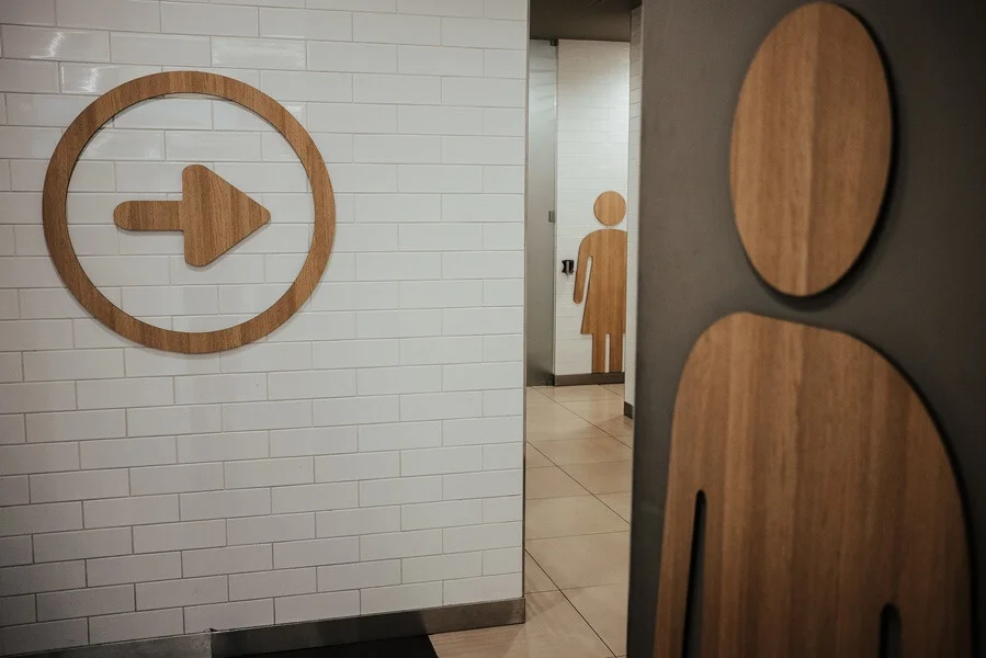 A restroom directional signage on tiled wall.